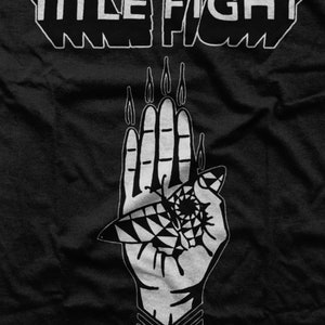 May include: Black and white graphic design of a hand with flames coming from the fingers. The hand is holding a stylized eye with a geometric pattern. The text "WE FIGHT" is above the hand.