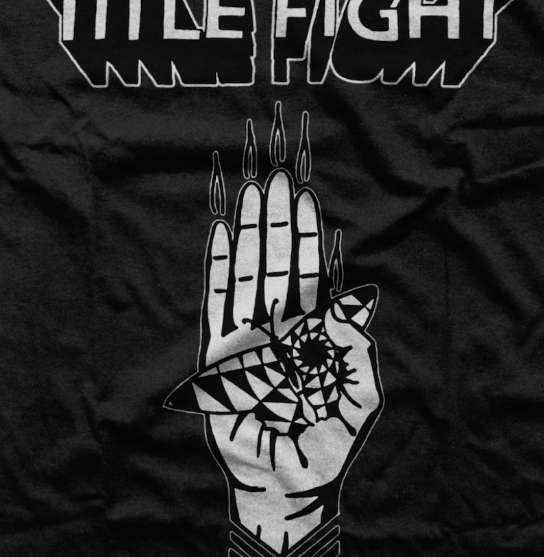 May include: Black and white graphic design of a hand with flames coming from the fingers. The hand is holding a stylized eye with a geometric pattern. The text "WE FIGHT" is above the hand.
