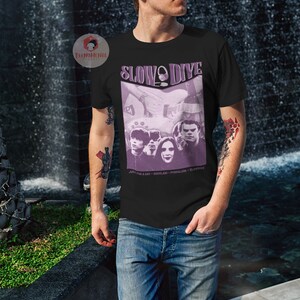 May include: A black t-shirt featuring a purple graphic of the band Slowdive. The graphic includes the band members and the text "Slowdive" in a purple circle. The text "Just for a Day - Souvlaki - Pygmalion - Slowdive" is printed below the graphic.