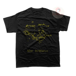 Könnte beinhalten: Schwarzes T-Shirt mit einer gelben Linienzeichnung eines Gesichts und dem Text "Mac DeMarco" in Gelb.