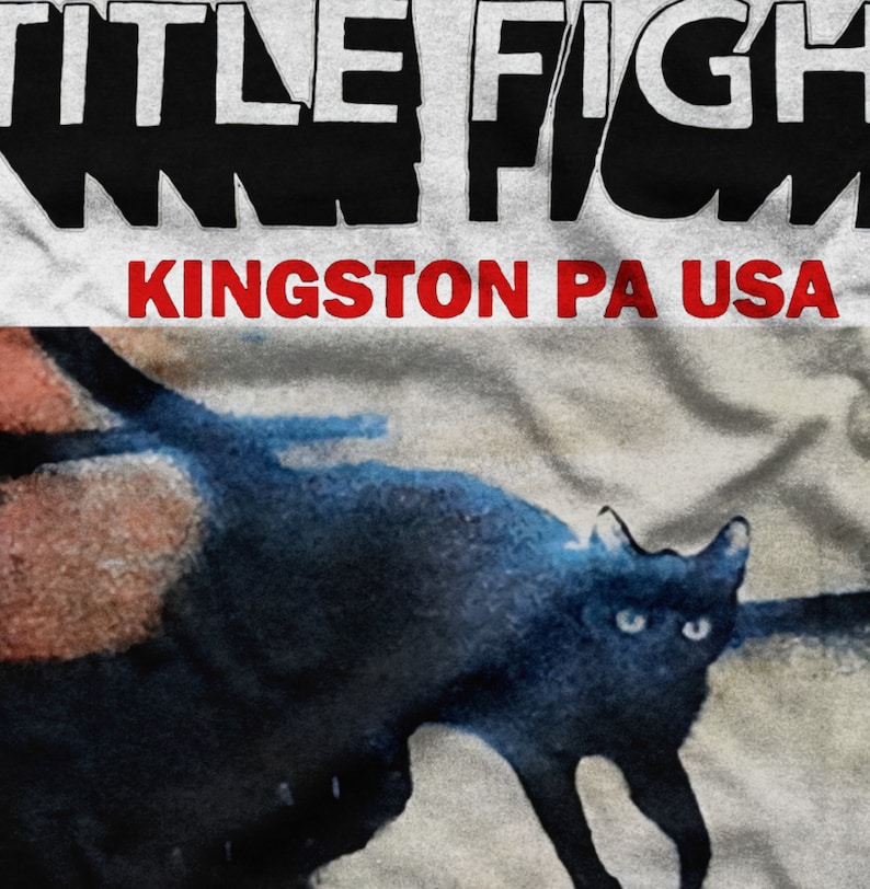 Pu&ograve; includere: Un gatto nero con gli occhi verdi cammina su una superficie bianca. Il testo "TITLE FIGHT KINGSTON PA USA" &egrave; stampato in nero e rosso sulla superficie.