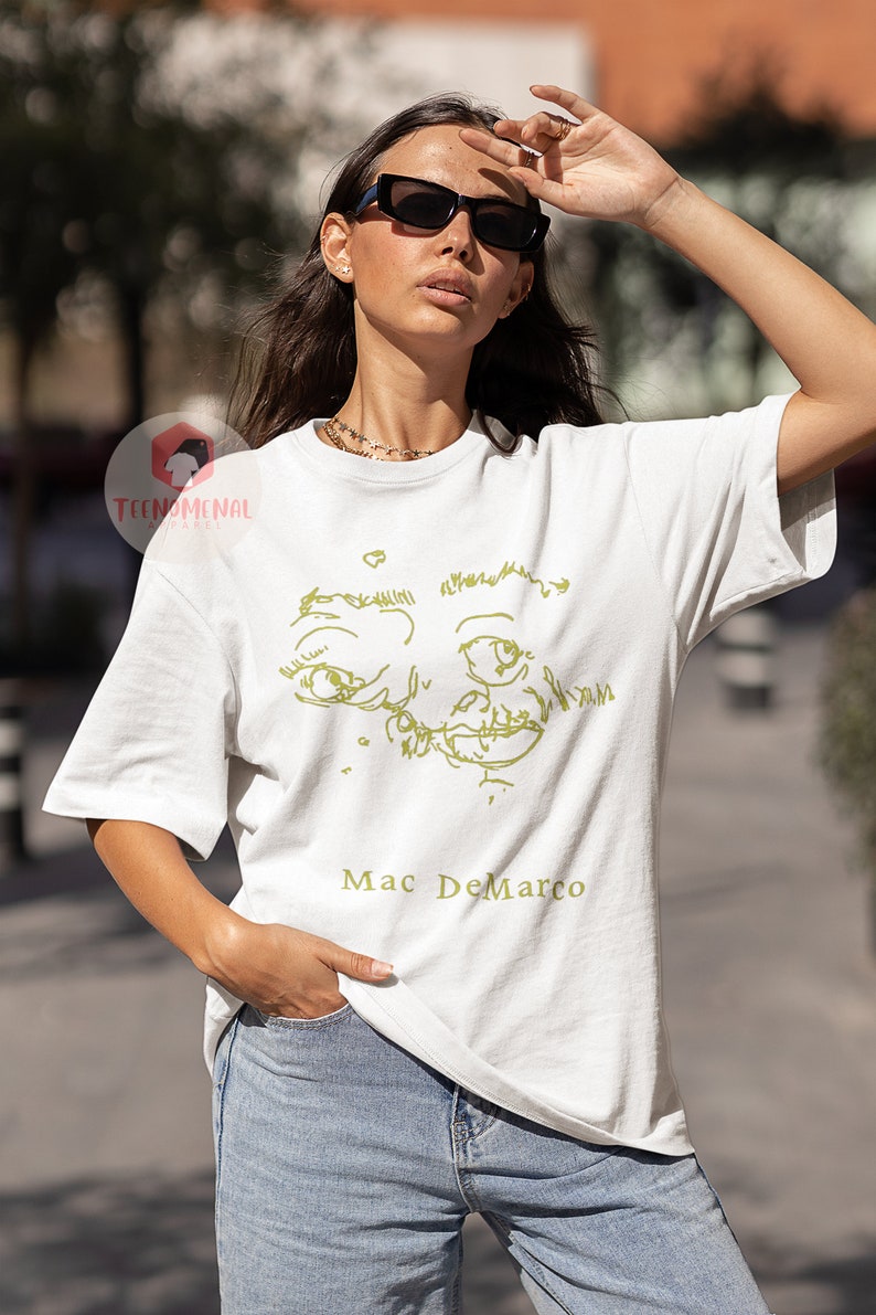 Puede incluir: Camiseta blanca con un dibujo de l&iacute;nea verde de una cara y el texto "Mac DeMarco" impreso en la parte delantera.