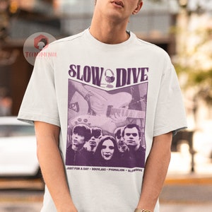 May include: White t-shirt featuring a purple graphic of the band Slowdive. The graphic includes the band's name, a photo of the band members, and the text "Just for a Day - Souvlaki - Pygmalion - Slowdive".