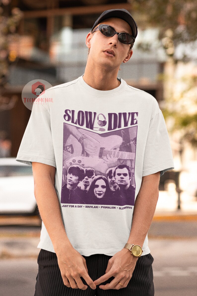 May include: White t-shirt featuring a purple graphic of the band Slowdive. The graphic includes the band's name, a photo of the band members, and the text "Just for a Day - Souvlaki - Pygmalion - Slowdive".