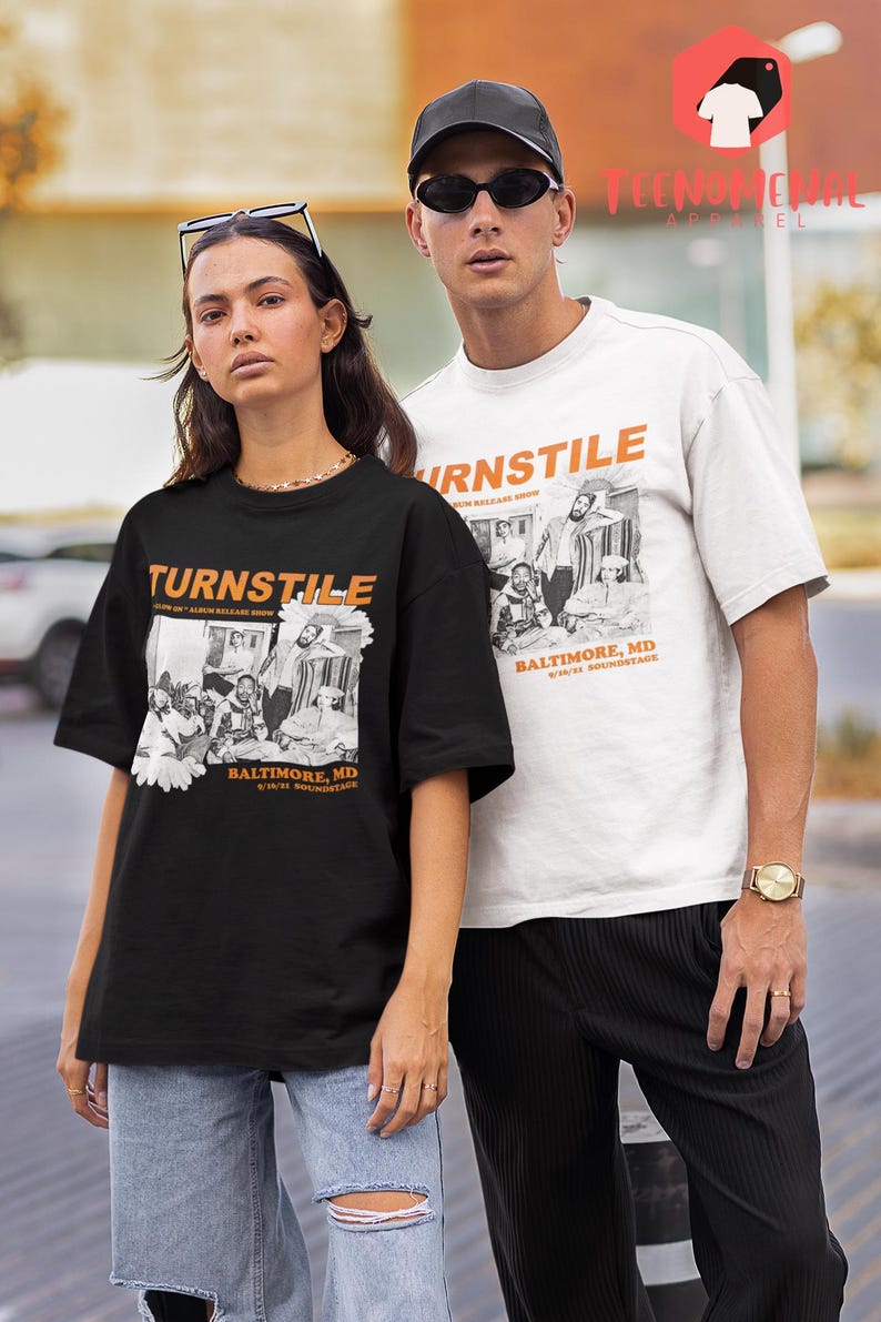 May include: Two people wearing black and white t-shirts with a band graphic and the text "Turnstile" and "Baltimore, MD". The graphic features a black and white photo of a band with the text "Turnstile" and "Baltimore, MD" in orange.