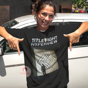 May include: Black t-shirt with the text "TITLE FIGHT HYPERVIEW" in white and a graphic of a person standing in front of a geometric pattern.