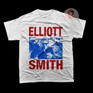 May include: White t-shirt with a red and blue graphic print of Elliott Smith. The graphic features a photo of Elliott Smith in a blue jacket, with the text "ELLIOTT SMITH" in red letters.