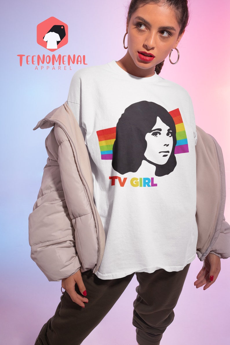 May include: White t-shirt featuring a black and white illustration of a woman with a rainbow behind her and the text "TV GIRL" underneath.