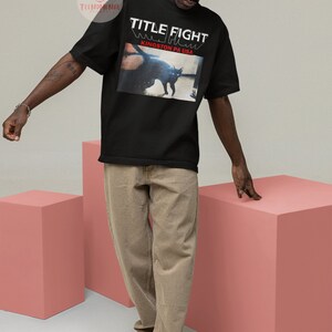Pu&ograve; includere: Una maglietta nera con la scritta "TITLE FIGHT" e "KINGSTON PA USA" stampata sul davanti. La maglietta presenta un'immagine in bianco e nero di un gatto.