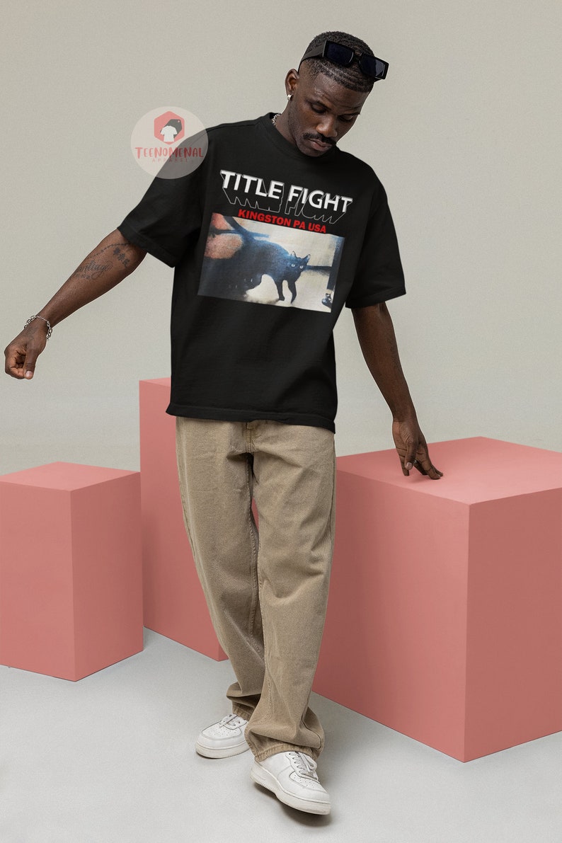 Pu&ograve; includere: Una maglietta nera con la scritta "TITLE FIGHT" e "KINGSTON PA USA" stampata sul davanti. La maglietta presenta un'immagine in bianco e nero di un gatto.