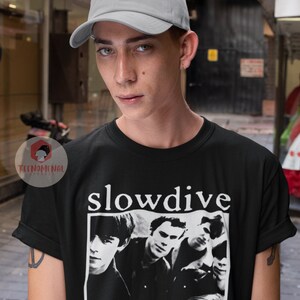 May include: A black t-shirt with a white print of a band called "slowdive". The band members are pictured in black and white. The person wearing the shirt is also wearing a gray baseball cap.