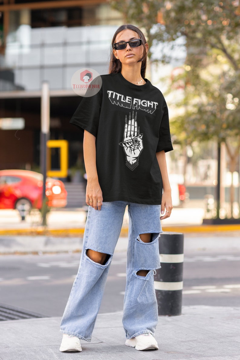 May include: A black t-shirt with a white graphic of a hand with an eye and the text "TITLE FIGHT" printed on the front.