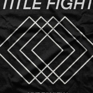 Op de afbeelding: Zwart T-shirt met een wit grafisch ontwerp van overlappende vierkanten en de tekst "TITLE FIGHT" en "HYPERVIEW".