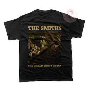 May include: Black t-shirt featuring a vintage-style image of The Smiths band members. The text "THE SMITHS" and "THE WORLD WON'T LISTEN" is printed in gold on the shirt.