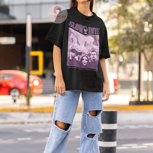 May include: A black t-shirt with a purple graphic print of a band called "Slowdive". The graphic features a band photo and the text "Just for a Day - Souvlaki - Pygmalion -  Slowdive".
