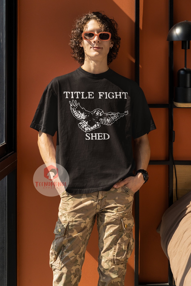 Puede incluir: Una camiseta negra con un gr&aacute;fico blanco de un b&uacute;ho volando con el texto "TITLE FIGHT SHED" impreso en la parte delantera.