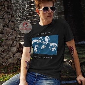Puede incluir: Una camiseta negra con una impresi&oacute;n blanca de la banda Slowdive. La impresi&oacute;n presenta un fondo azul con una foto de los miembros de la banda y el texto "souvlaki (1993)".