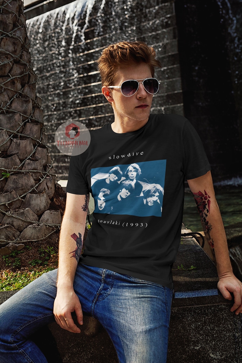 Puede incluir: Una camiseta negra con una impresi&oacute;n blanca de la banda Slowdive. La impresi&oacute;n presenta un fondo azul con una foto de los miembros de la banda y el texto "souvlaki (1993)".