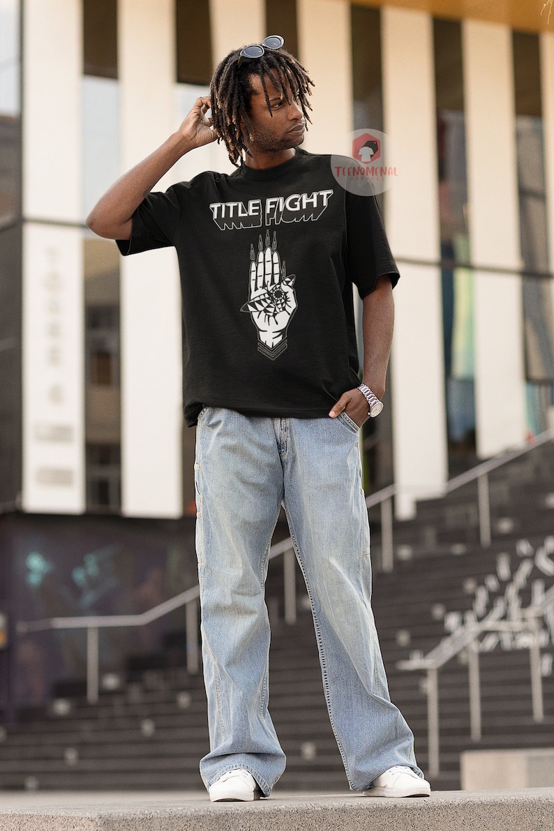 May include: A black t-shirt with a white graphic of a hand with an eye and the text "TITLE FIGHT" printed on the front.