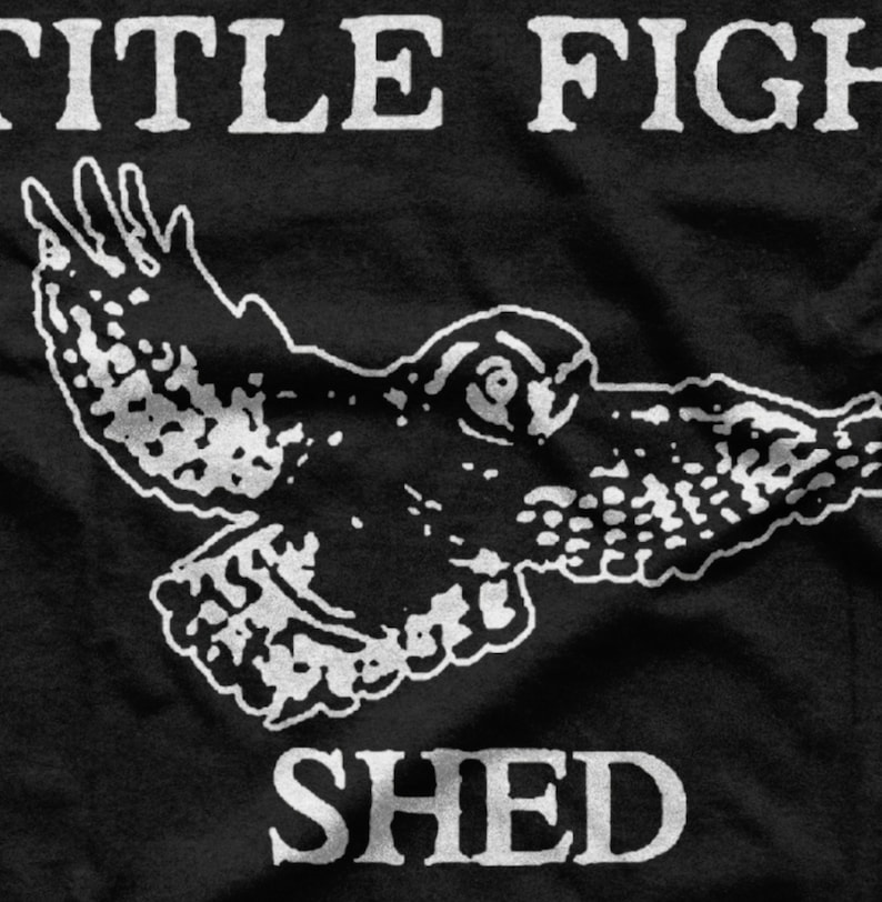 Puede incluir: Camiseta negra con un gr&aacute;fico blanco de un p&aacute;jaro en vuelo y el texto "TITLE FIGHT SHED" debajo.