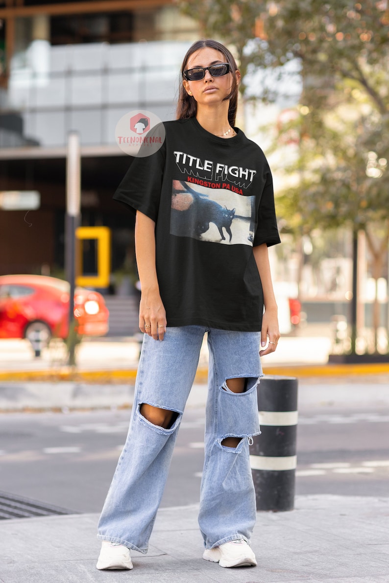 Pu&ograve; includere: Maglietta nera con una stampa grafica di un gatto nero e il testo "TITLE FIGHT" e "KINGSTON PA USA".