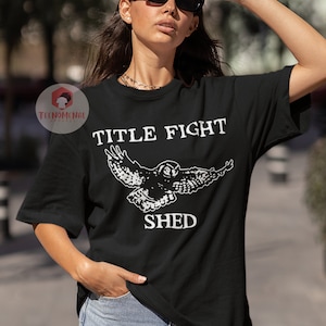 Puede incluir: Camiseta negra con un gr&aacute;fico blanco de un b&uacute;ho en vuelo y el texto "TITLE FIGHT SHED".