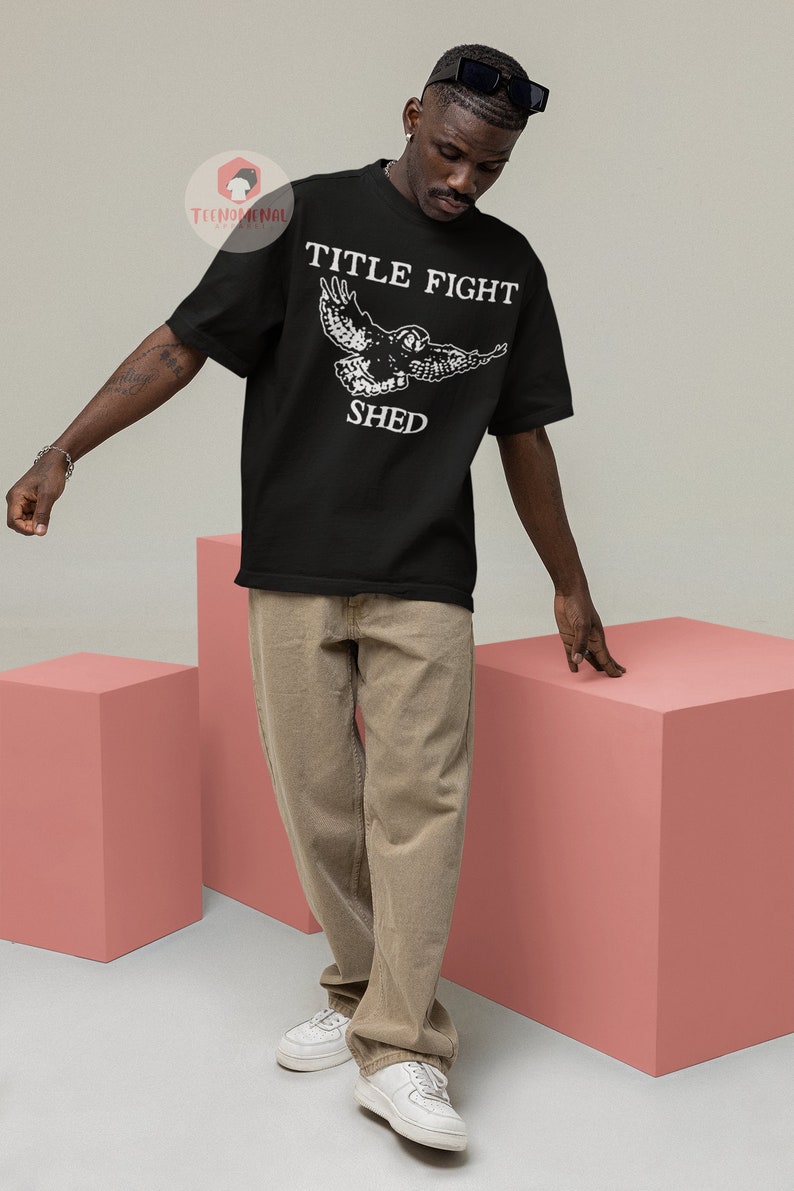 Puede incluir: Una camiseta negra con un gr&aacute;fico blanco de un b&uacute;ho volando con el texto "TITLE FIGHT SHED" impreso en la parte delantera.