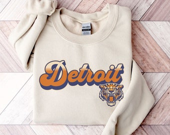 May include: A sand-colored sweatshirt with a retro-style graphic of the word "Detroit" in orange and blue with a tiger head graphic.