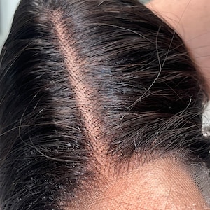 May include: Close-up of a dark brown human hair wig with a lace front. The lace is visible and the hair is parted in the middle.