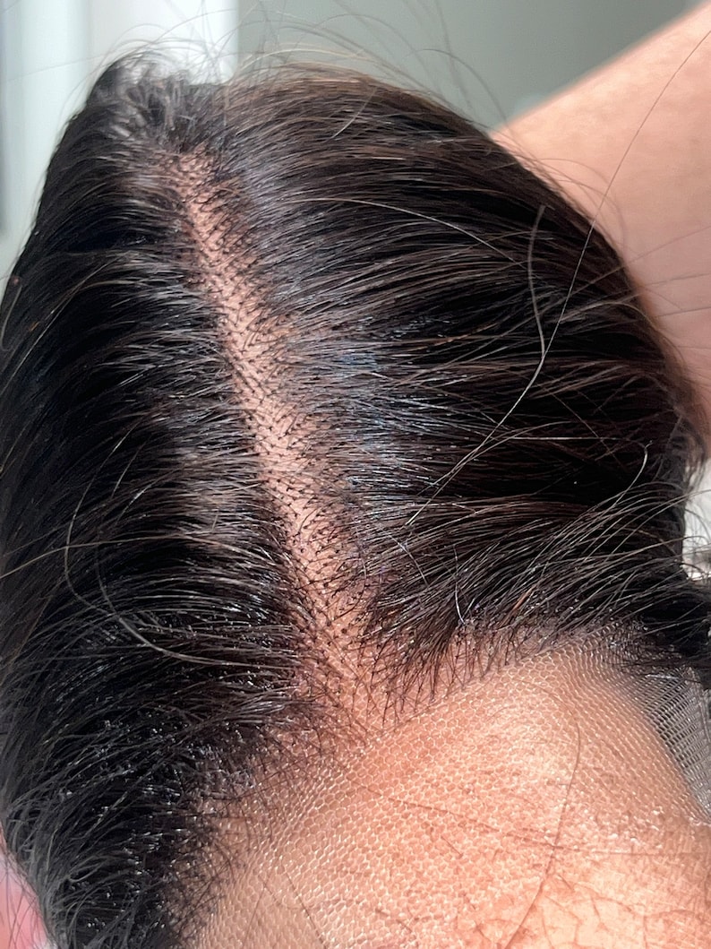 May include: Close-up of a dark brown human hair wig with a lace front. The lace is visible and the hair is parted in the middle.