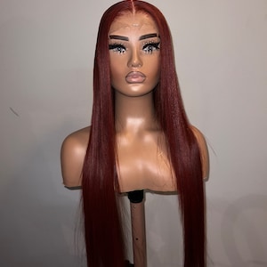 May include: A long, straight, auburn-colored human hair wig with a lace front. The wig is on a mannequin head.