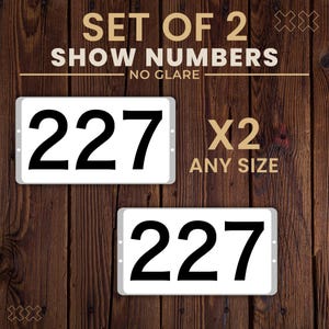 May include: Two white rectangular show number plates with the number 227 in bold black font. The text "SET OF 2 SHOW NUMBERS" and "NO GLARE" are at the top. The text "X2 ANY SIZE" is to the right.