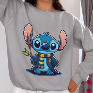May include: Gray sweatshirt with a blue Stitch character wearing a yellow and blue scarf and holding a brown stick. Stitch is wearing a blue robe with a yellow and red crest.