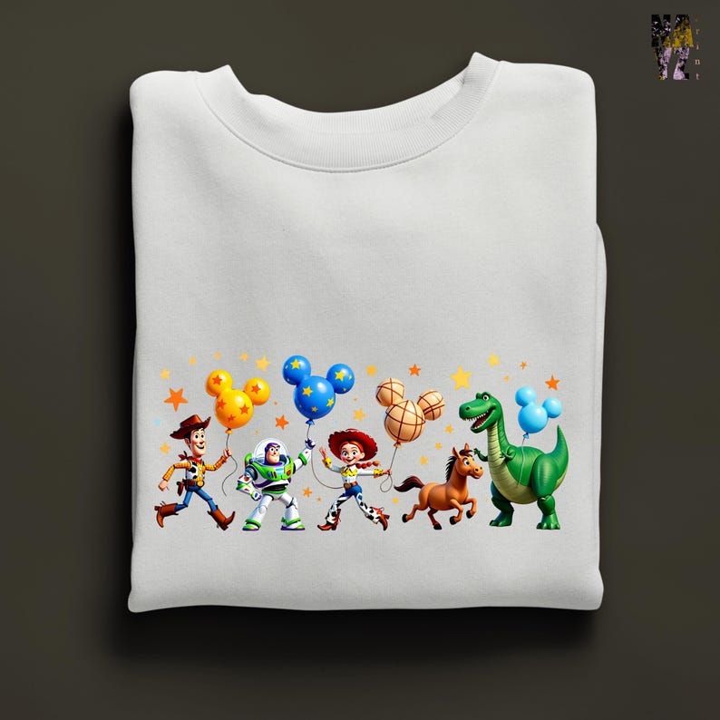 Puede incluir: Sudadera blanca con un gr&aacute;fico colorido de personajes animados, incluyendo un vaquero, un guardabosques espacial y un dinosaurio, cada uno sosteniendo ramos de globos. El dise&ntilde;o incluye estrellas, ideal para fans de pel&iacute;culas animadas.