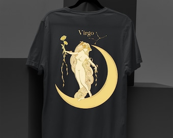 May include: Dark gray t-shirt featuring a gold illustration of a woman standing on a crescent moon, holding flowers. The word "Virgo" is above the illustration, with a constellation design. The shirt is hanging on a black hanger.