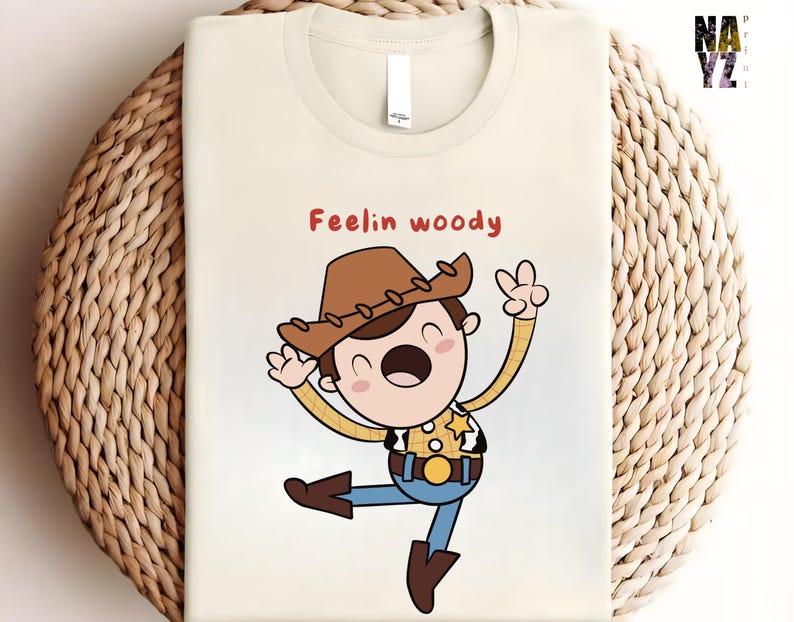 Puede incluir: Una camiseta blanca con una ilustraci&oacute;n de dibujos animados de Woody de Toy Story. La ilustraci&oacute;n muestra a Woody con su caracter&iacute;stico sombrero de vaquero, chaleco y una expresi&oacute;n alegre. El texto "Feelin' Woody" est&aacute; impreso sobre la ilustraci&oacute;n.
