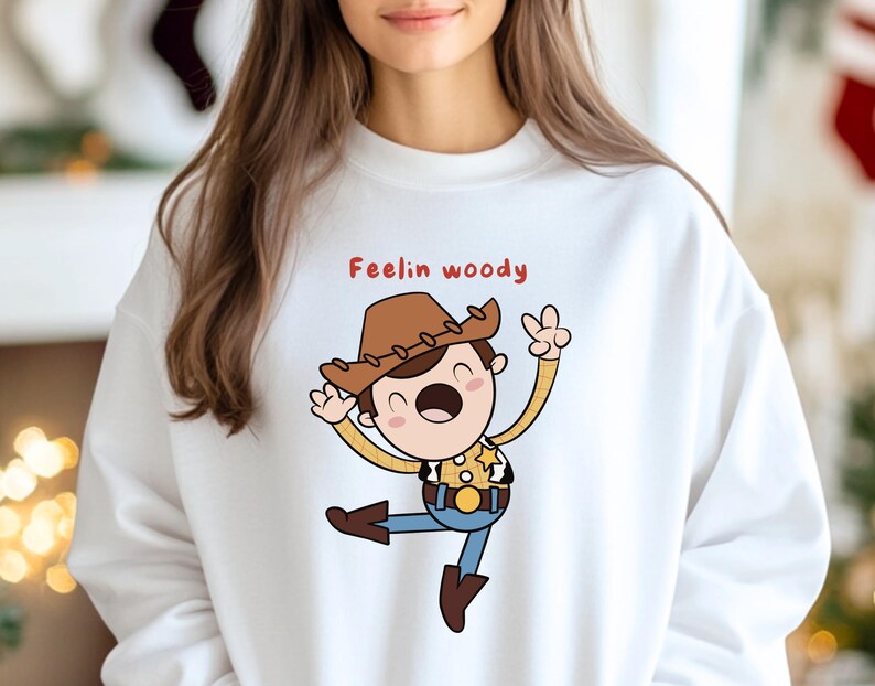 Puede incluir: Sudadera blanca con una ilustraci&oacute;n de dibujos animados de Woody de Toy Story. El texto "Feelin Woody" est&aacute; impreso en rojo sobre la ilustraci&oacute;n.