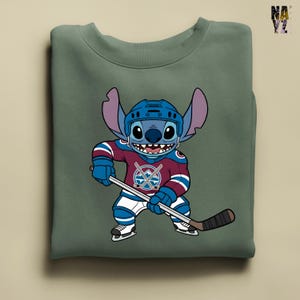 Puede incluir: Sudadera verde con un personaje de dibujos animados con uniforme y casco de hockey, sosteniendo un palo de hockey. El uniforme es granate, azul y blanco.