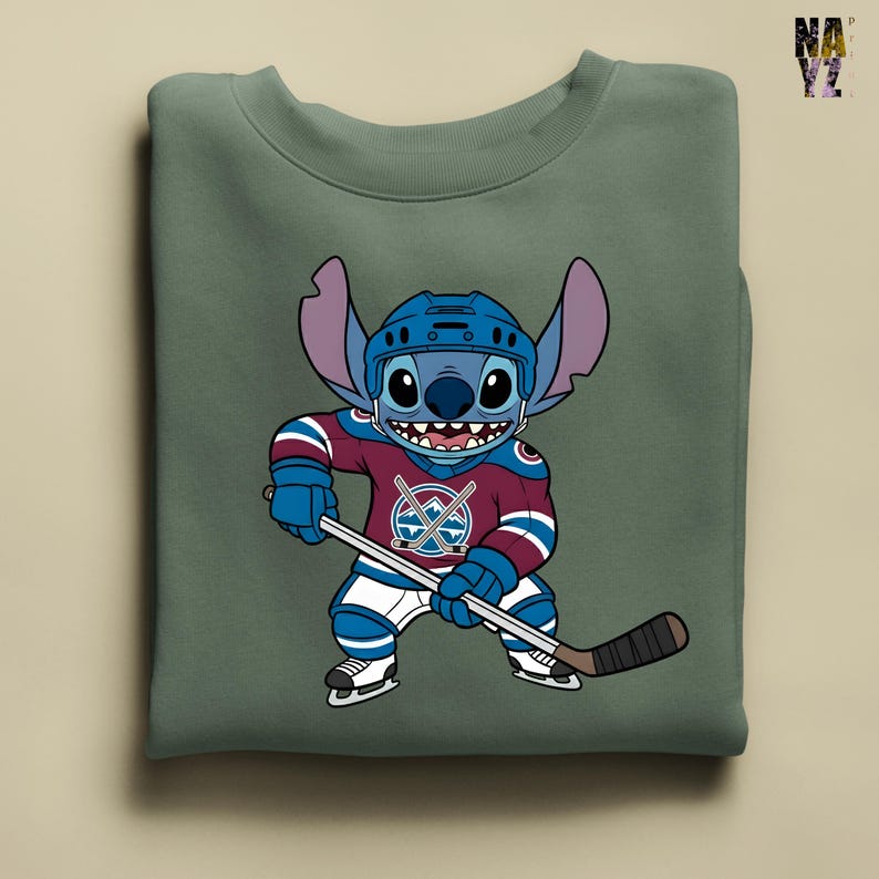 Puede incluir: Sudadera verde con un personaje de dibujos animados con uniforme y casco de hockey, sosteniendo un palo de hockey. El uniforme es granate, azul y blanco.