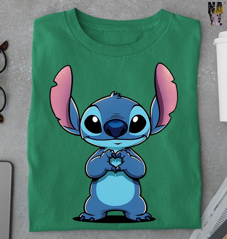 May include: Green t-shirt featuring a cartoon illustration of Stitch from Lilo & Stitch. The blue character is making a heart shape with its hands. The shirt is folded and has a crew neck.