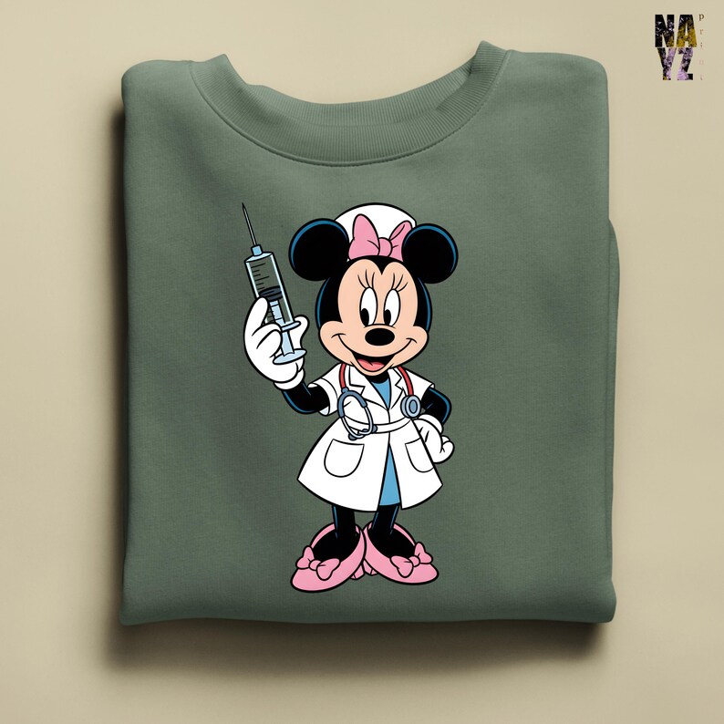 Peut inclure: Sweat-shirt vert sauge avec Minnie Mouse en infirmi&egrave;re, tenant une seringue. Minnie porte une blouse blanche, des chaussures roses et un bonnet d'infirmi&egrave;re avec un n&oelig;ud rose. Le sweat-shirt a un col rond.
