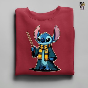 May include: A maroon sweatshirt featuring a cartoon character, Stitch, dressed in a wizard's robe and scarf. The blue character holds a wand, with large ears and a detailed design. The scarf is yellow and black, and the robe is dark blue.