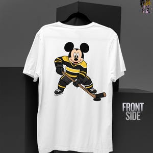 May include: White t-shirt featuring a cartoon Mickey Mouse character in a hockey uniform with black and yellow stripes, holding a hockey stick. The words "FRONT SIDE" are printed on the right side of the shirt.