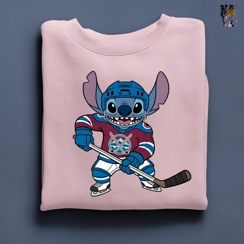Puede incluir: Sudadera rosa claro con un personaje de dibujos animados Stitch con uniforme de hockey. Stitch lleva un casco azul y sostiene un palo de hockey. El uniforme es burdeos, azul y blanco, con un logotipo del equipo en el pecho.