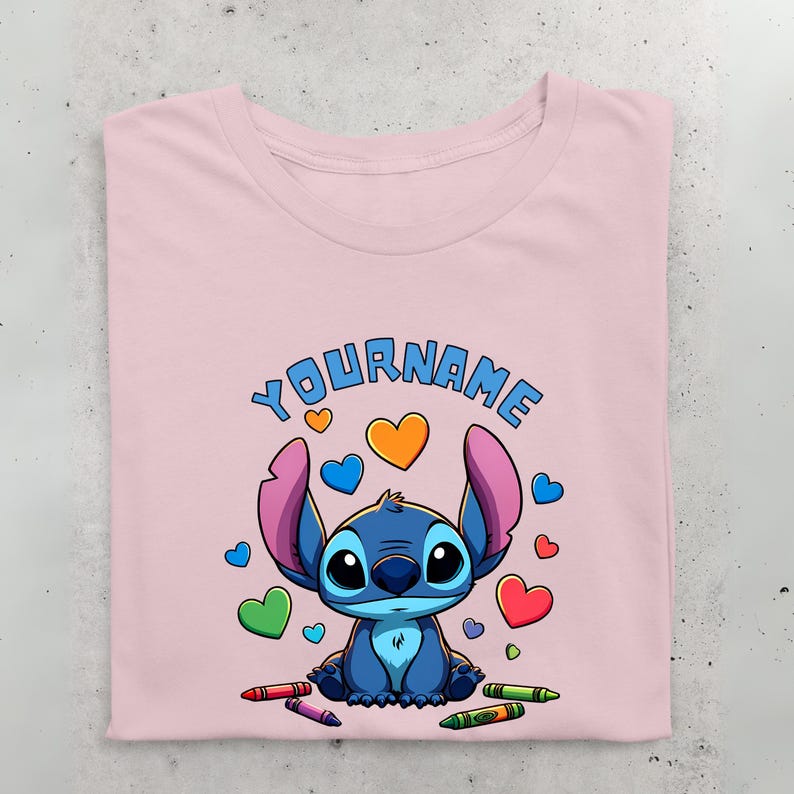 K&ouml;nnte beinhalten: Rosa T-Shirt mit einer blauen Stitch-Figur aus Lilo & Stitch. Stitch ist von bunten Herzen und Buntstiften umgeben. Der Text "YOUR NAME" befindet sich &uuml;ber Stitch.