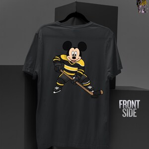 May include: Dark gray t-shirt featuring a cartoon Mickey Mouse character in a hockey uniform with black and yellow stripes, holding a hockey stick. The shirt has the words "FRONT SIDE" printed on the right side.