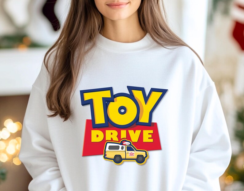 May include: White sweatshirt with a blue and yellow "Toy Drive" graphic featuring a cartoon toy truck.