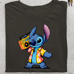 Op de afbeelding: Donkergrijs t-shirt met een stripfiguur, Stitch, die een gele boombox vasthoudt. Stitch is blauw met grote ogen en draagt een Hawaiiaans shirt met witte en oranje bloemen. Het shirt heeft een klassieke ronde hals.