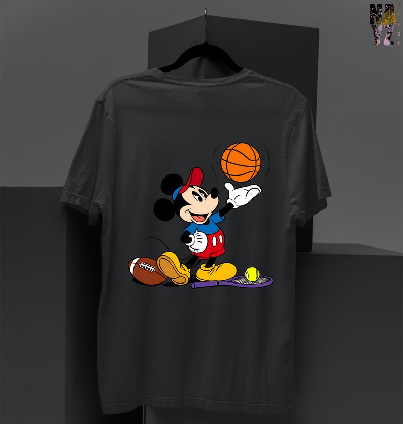 May include: Dark gray t-shirt featuring a cartoon Mickey Mouse character in a sports theme. Mickey is wearing a red hat, blue shirt, and red shorts, holding a basketball. A football, tennis racket, and tennis ball are also visible.