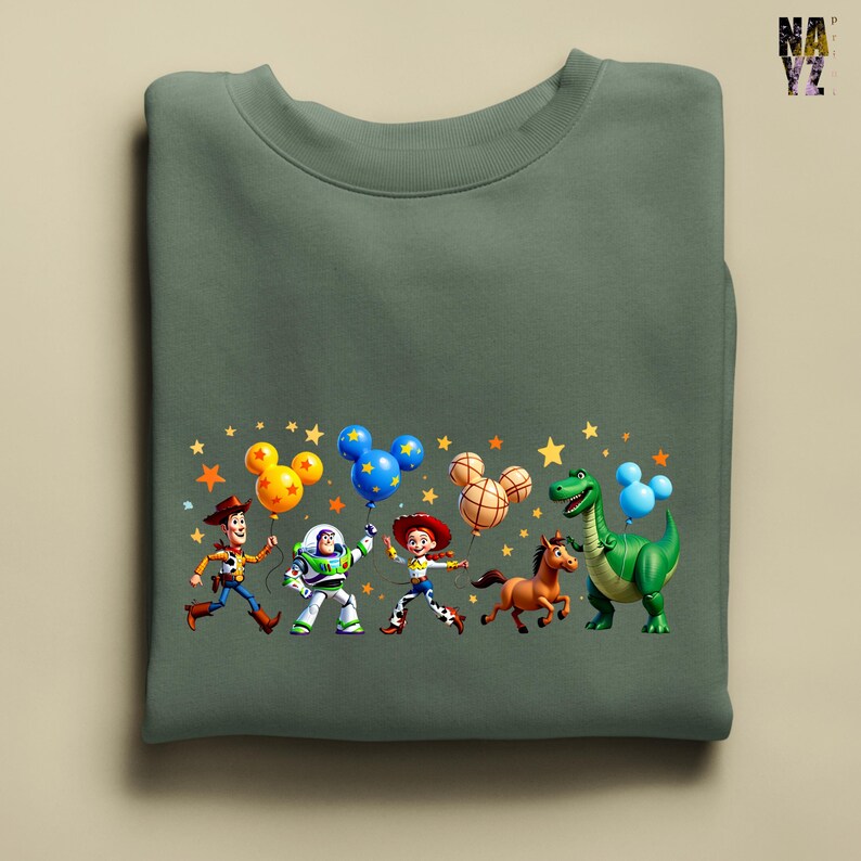 Puede incluir: Sudadera verde salvia con un gr&aacute;fico colorido de personajes de Toy Story sosteniendo globos con forma de Mickey Mouse. Woody, Buzz Lightyear, Jessie, un caballo y un dinosaurio est&aacute;n representados con estrellas.